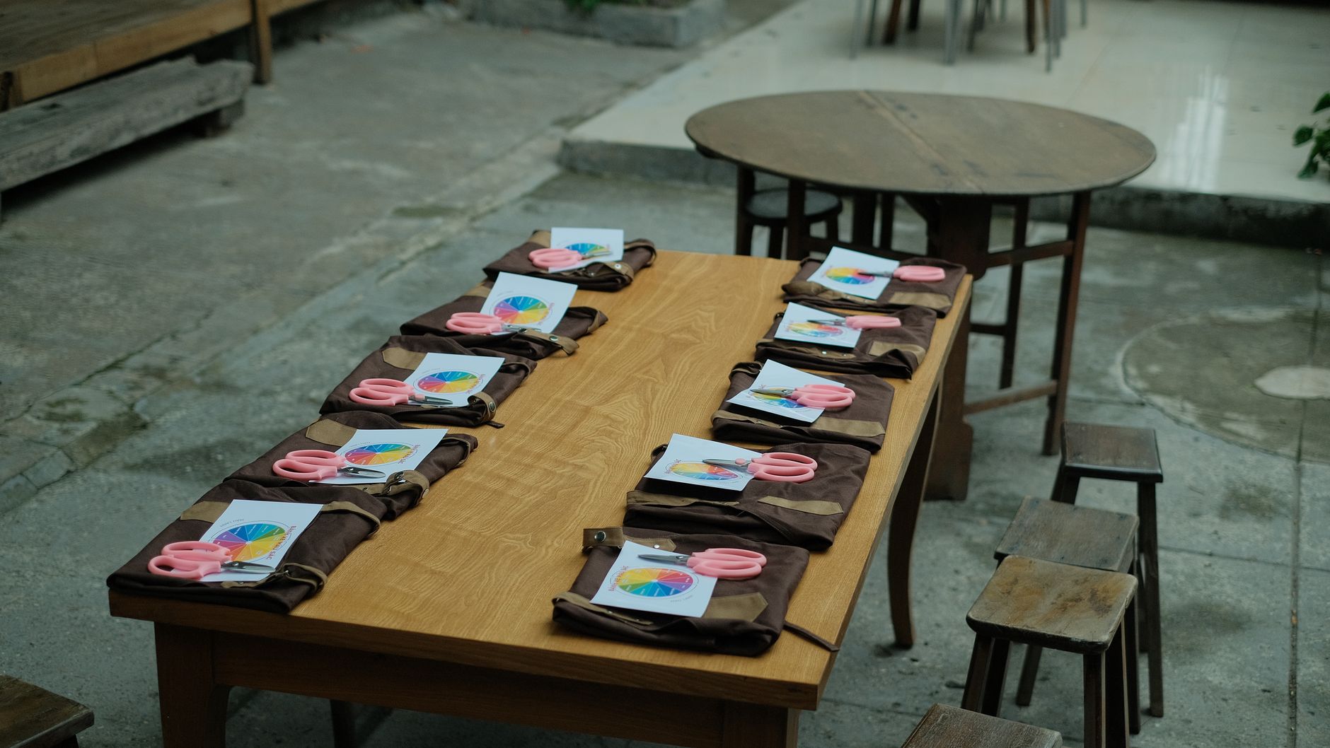 Outdoor setup with crafts supplies including pink scissors, aprons, and worksheets on a wooden table.