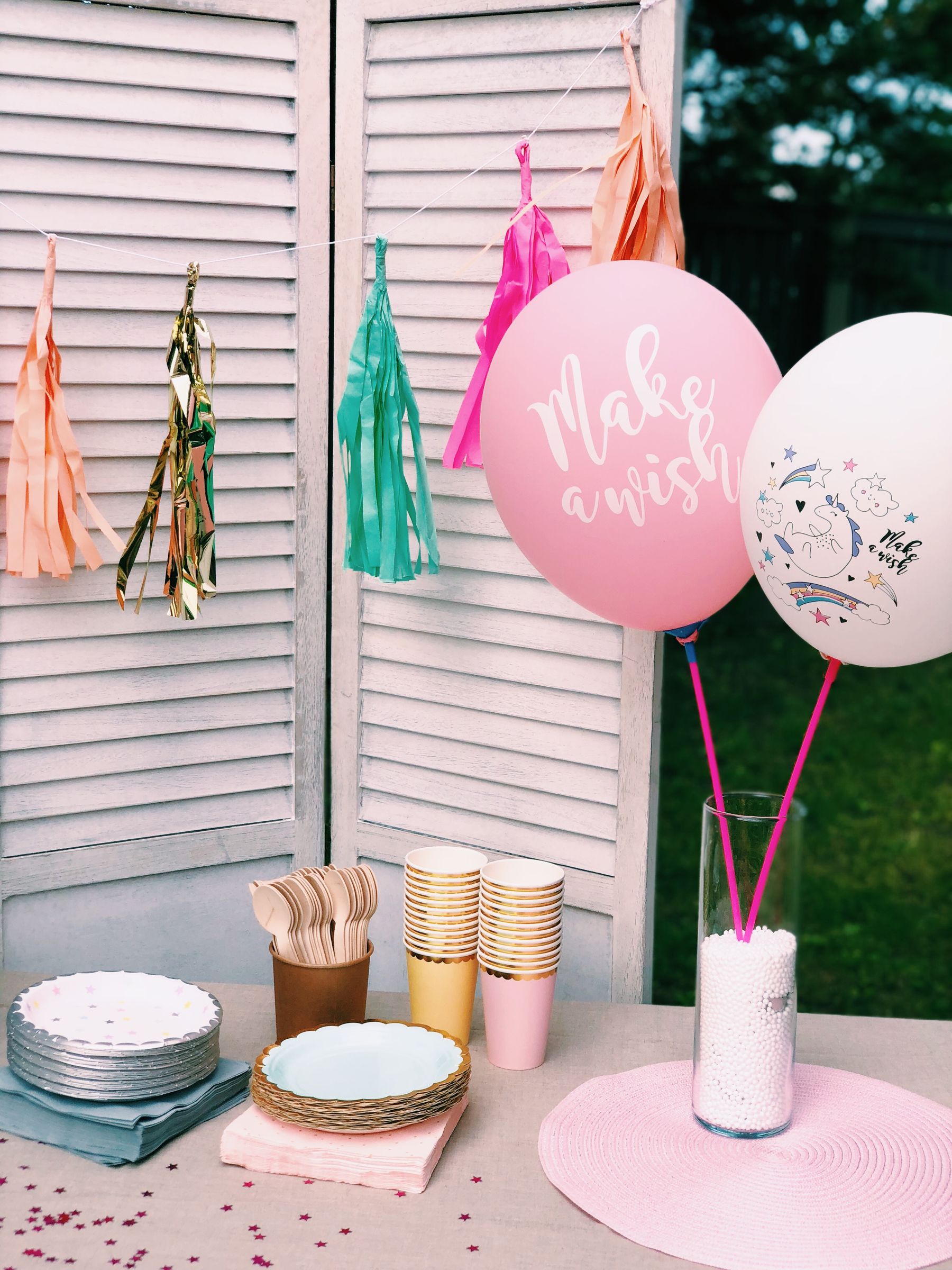 Garden party table arranged with paper plates, cups, garlands, and balloons