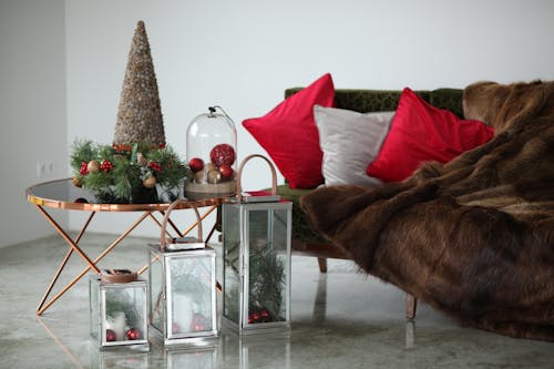 Trendy glass table with fur decorations and glass lanterns near couch with fur plaid during Xmas holidays