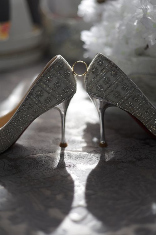 Free Elegant bridal heels adorned with rhinestones, creatively displaying a wedding ring under soft lighting. Stock Photo