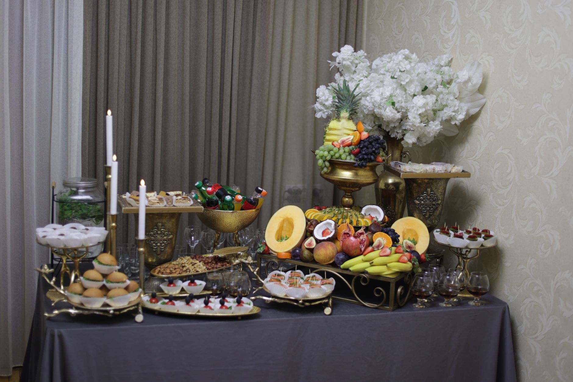 Opulent indoor buffet setup with fruits, desserts, and decor in an elegant setting.