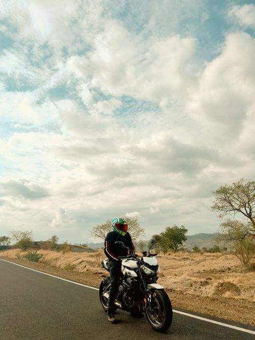 Free A rider pauses on a scenic road in Satara, Maharashtra, revealing vast skies and open terrain. Stock Photo