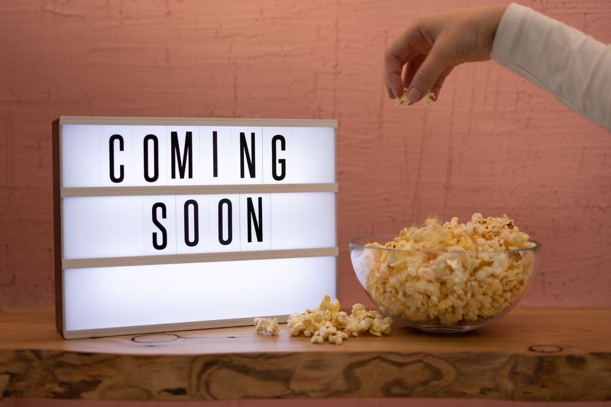 Hand reaching for popcorn with retro Coming Soon sign evoking nostalgic 80s movie nights