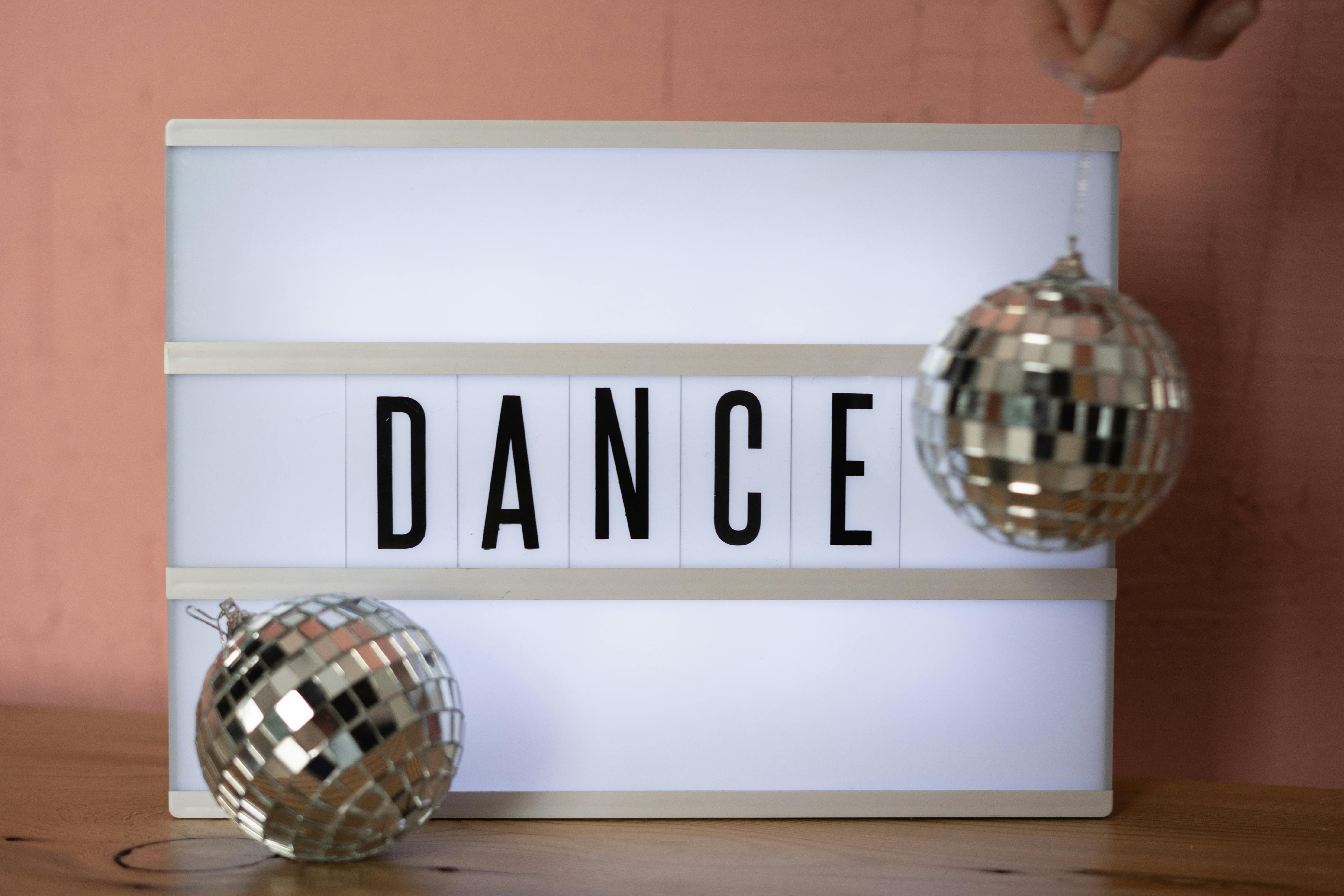 A lightbox displaying the word 'DANCE' with shiny disco balls on a wooden surface.