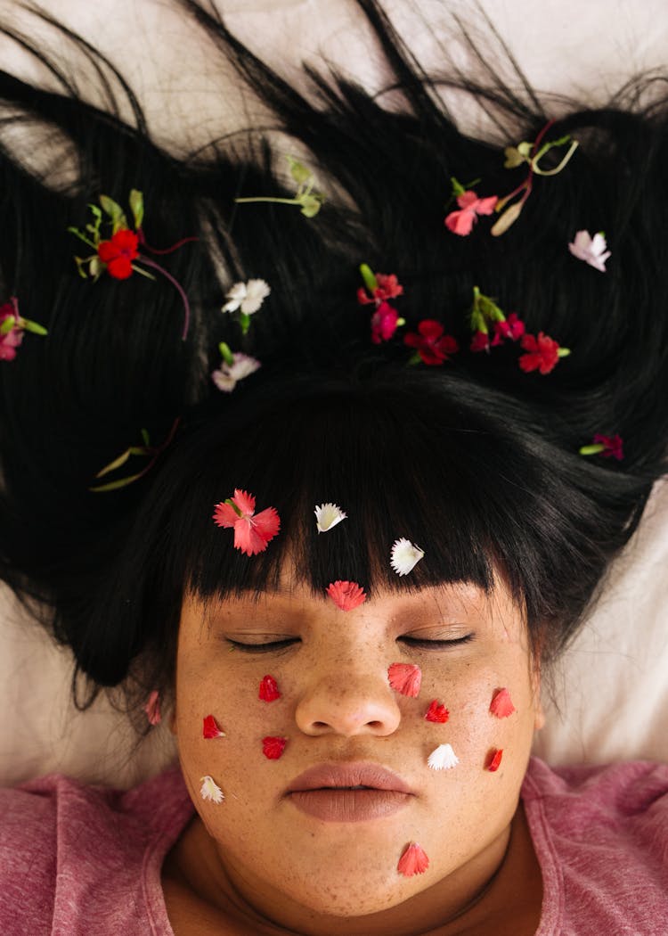 Sensual Young Overweight Ethnic Lady With Flower Petals And Closed Eyes Lying On Bed