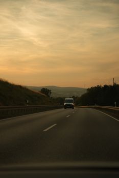 A tranquil highway drive amidst hills during a golden sunset, capturing nature's serene beauty.