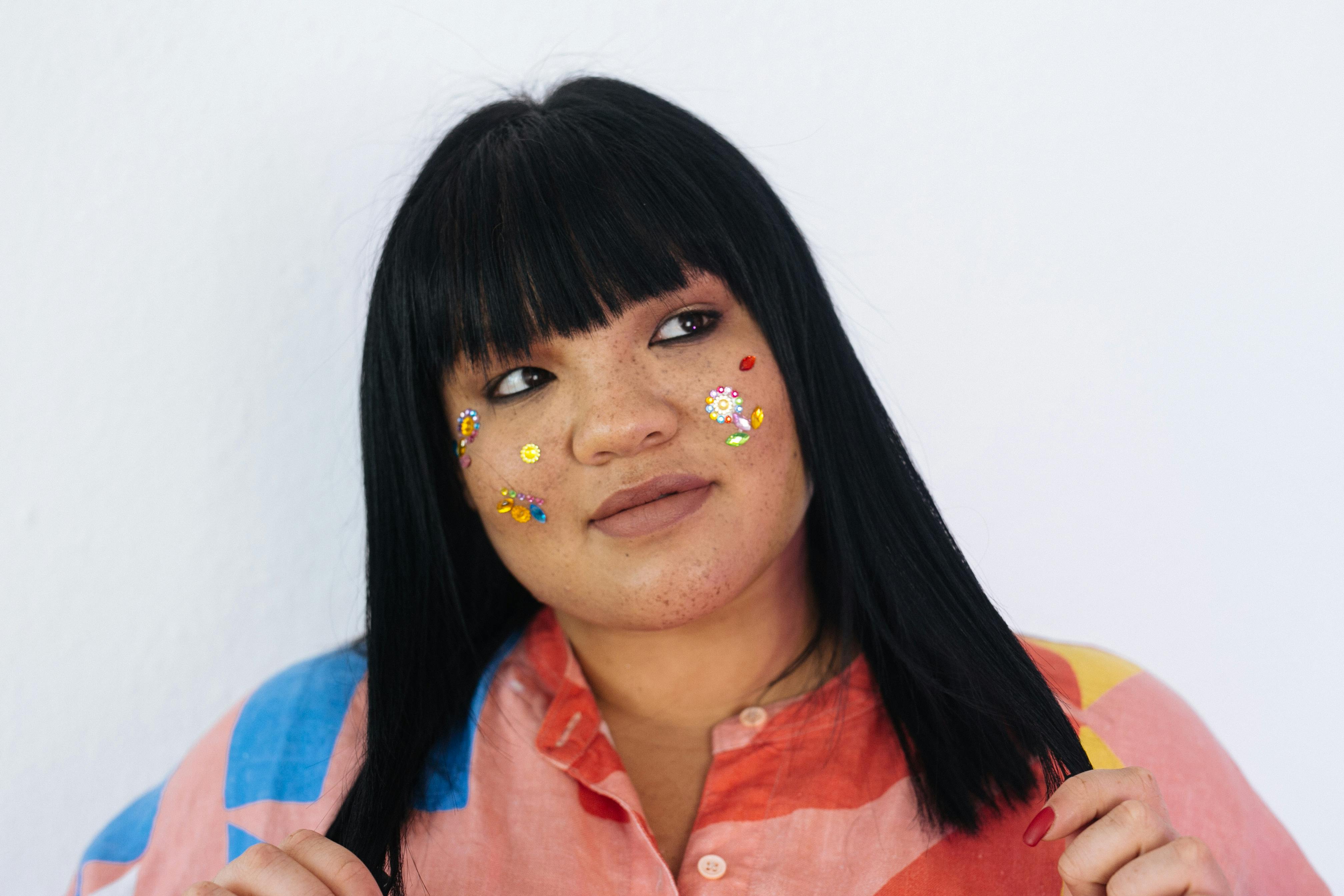 Young dreamy female with brunet hair and colorful makeup in bright shirt looking away