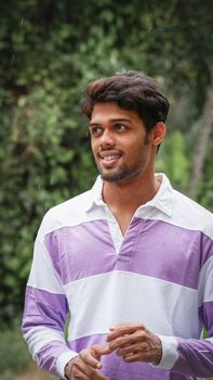 A young man enjoying a light rain outdoors, surrounded by lush greenery.