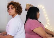 两个女人背靠背坐在室内，神情紧张，似有分歧