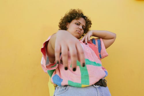Low angle of young facetious plus size African American female with curly hair standing in front of yellow wall and looking at camera