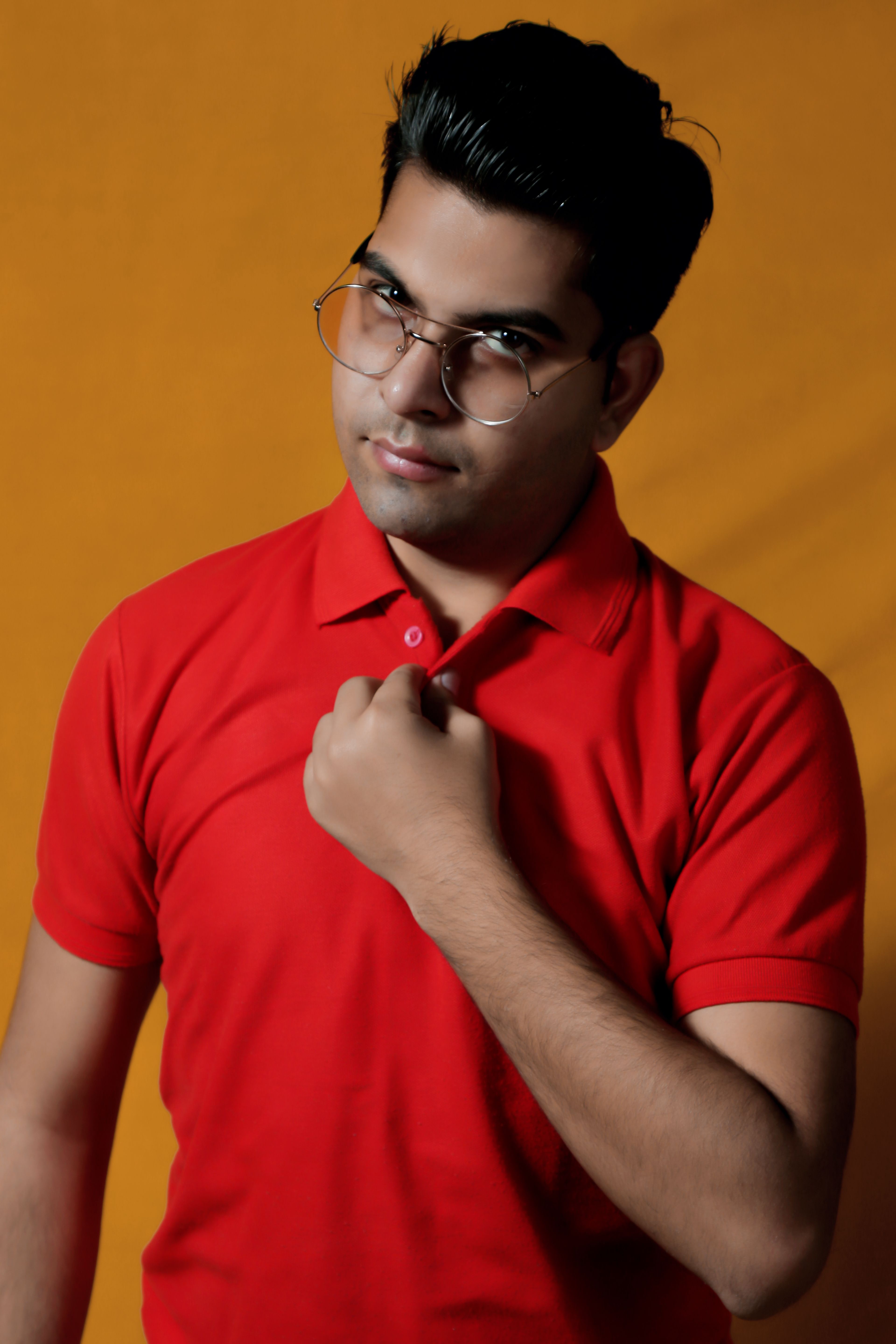Portrait of a confident man wearing a red polo shirt and glasses against an orange background.