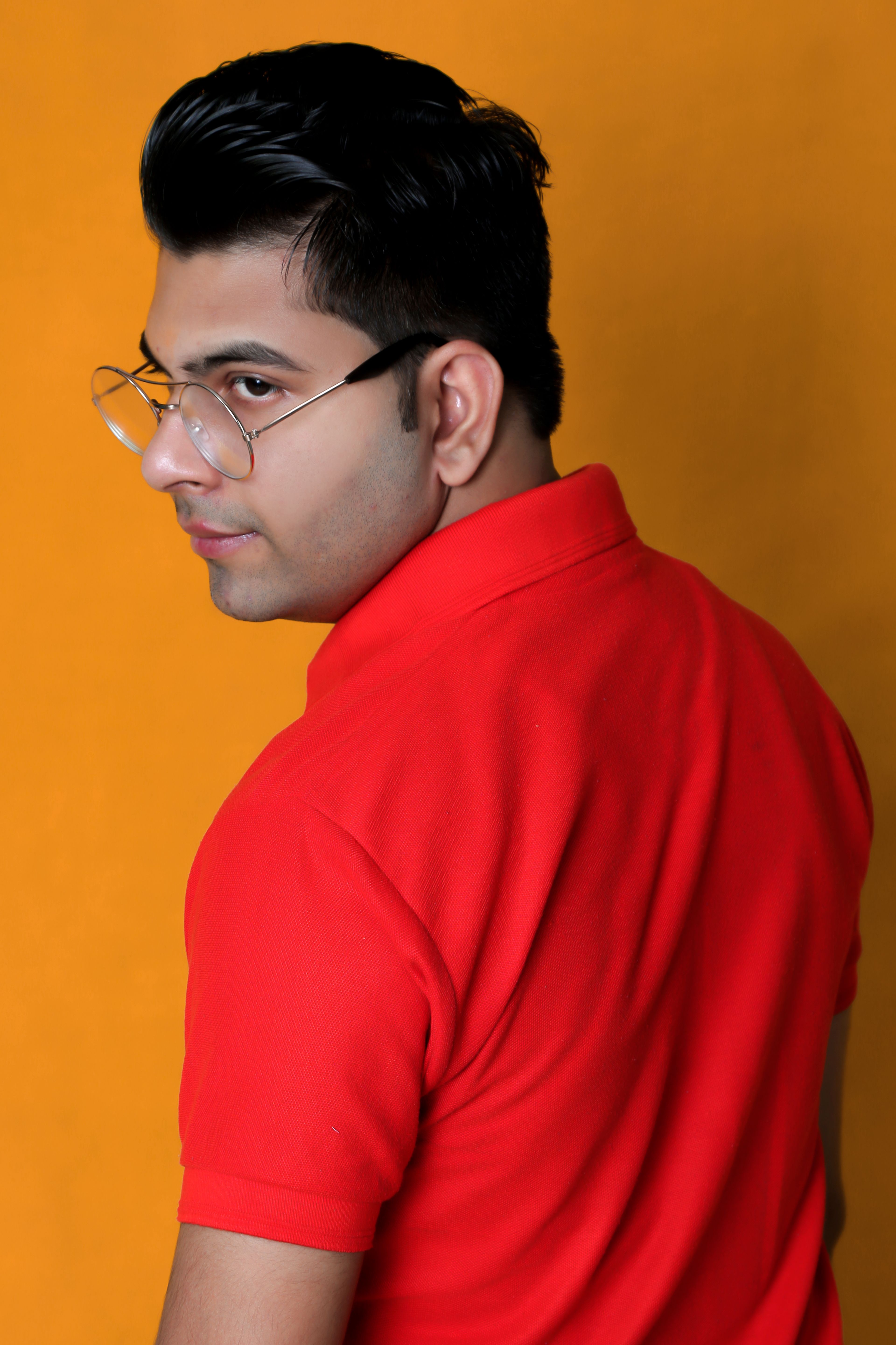 Portrait of a young man in glasses and a red polo against a vibrant orange backdrop.