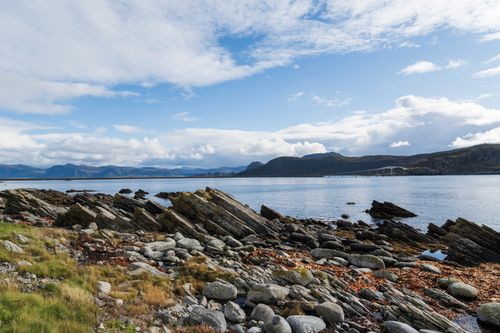 Free Panoramic view of Norway's rocky coastline and calm sea under a bright blue sky. Stock Photo