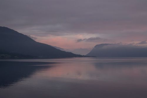 Free Calm pink and purple sunset over a Norwegian fjord with mountains and reflections. Stock Photo