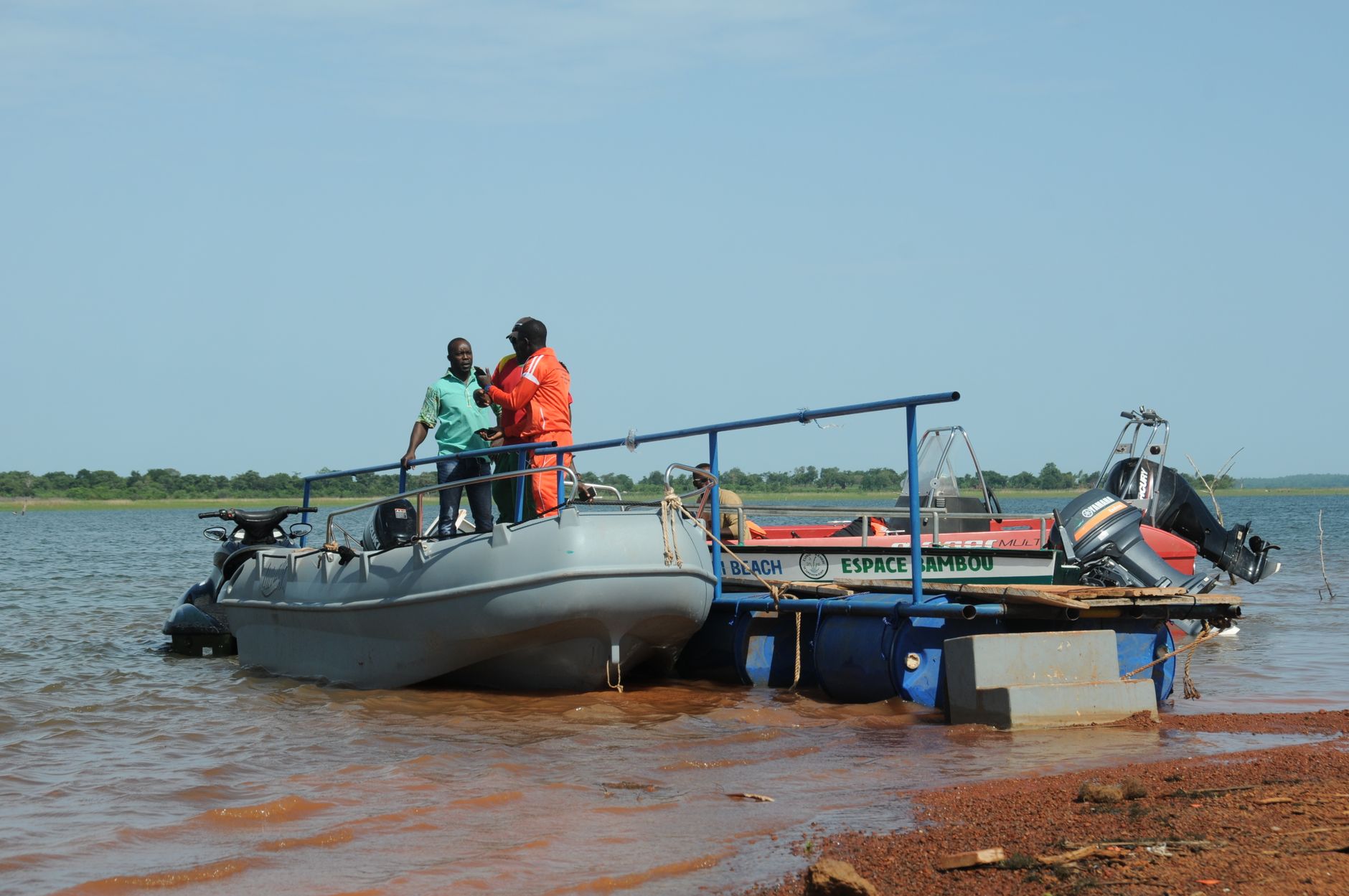 Two men on a boat discussing by a river bank in sunny Burkina Faso.