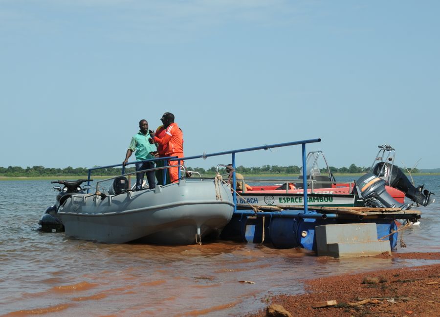 Two men on a boat discussing by a river bank in sunny Burkina Faso.