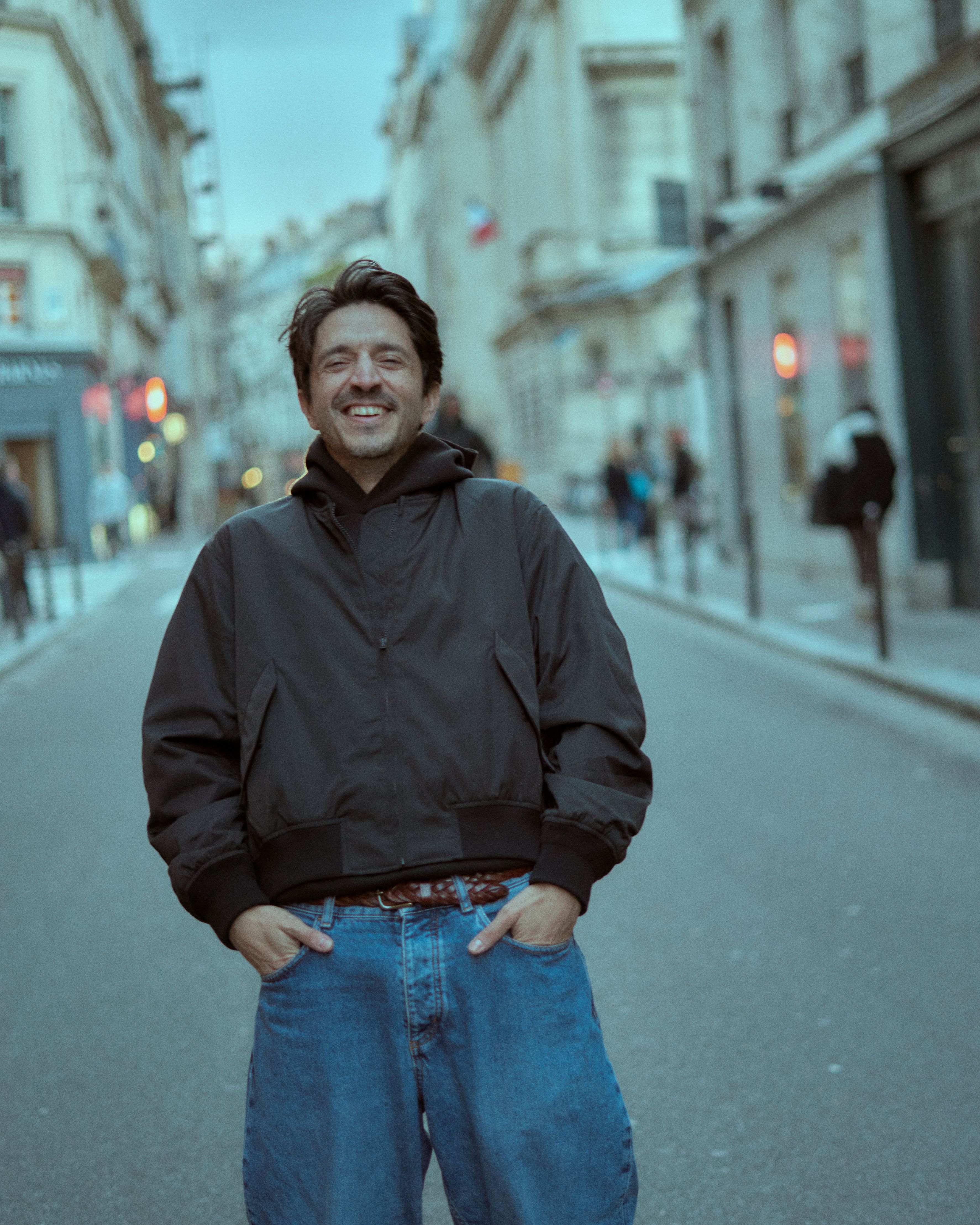 A joyful man in casual attire smiling on a European city street.
