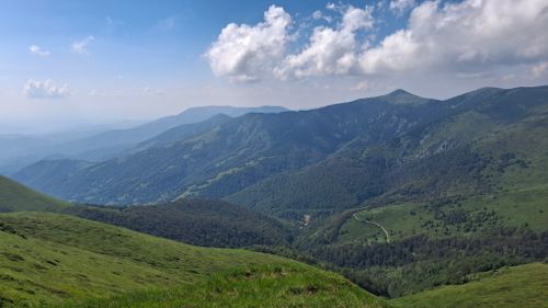 Free Breathtaking view of a mountain range with lush green valleys under a partly cloudy sky. Stock Photo