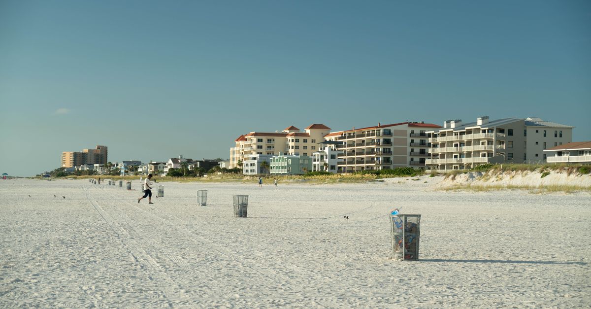 A wide sandy beach with beachfront residential buildings under a clear blue sky.