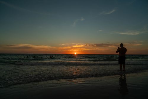 Free A serene beach sunset scene with a silhouette of a person capturing the view, creating a peaceful ambiance. Stock Photo