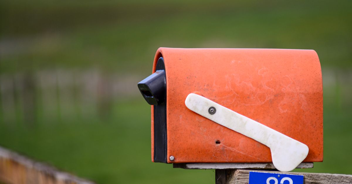 Orange mailbox on a wooden fence in Matamata, New Zealand, with a vivid landscape backdrop.
