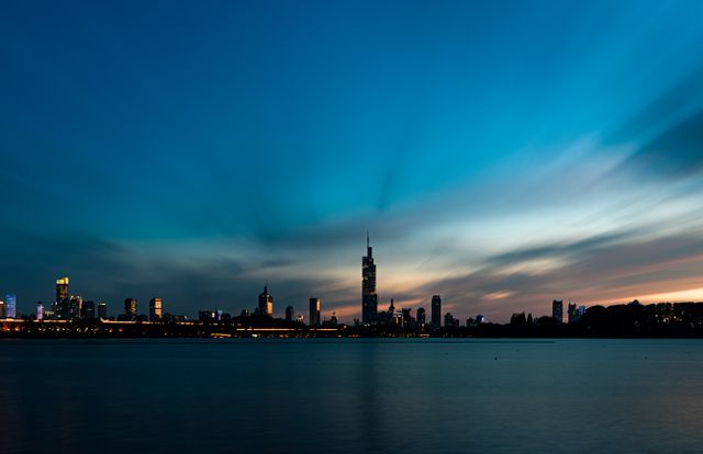 Beautiful city skyline view with dramatic twilight sky reflecting over calm waterfront, creating a serene urban landscape.