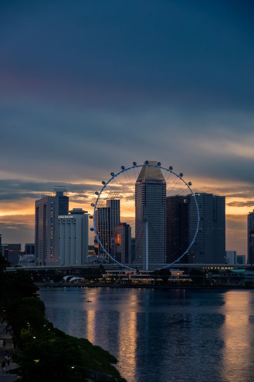 Free Dramatic sunset view of Singapore skyline with the iconic Ferris wheel and reflections on the water. Stock Photo
