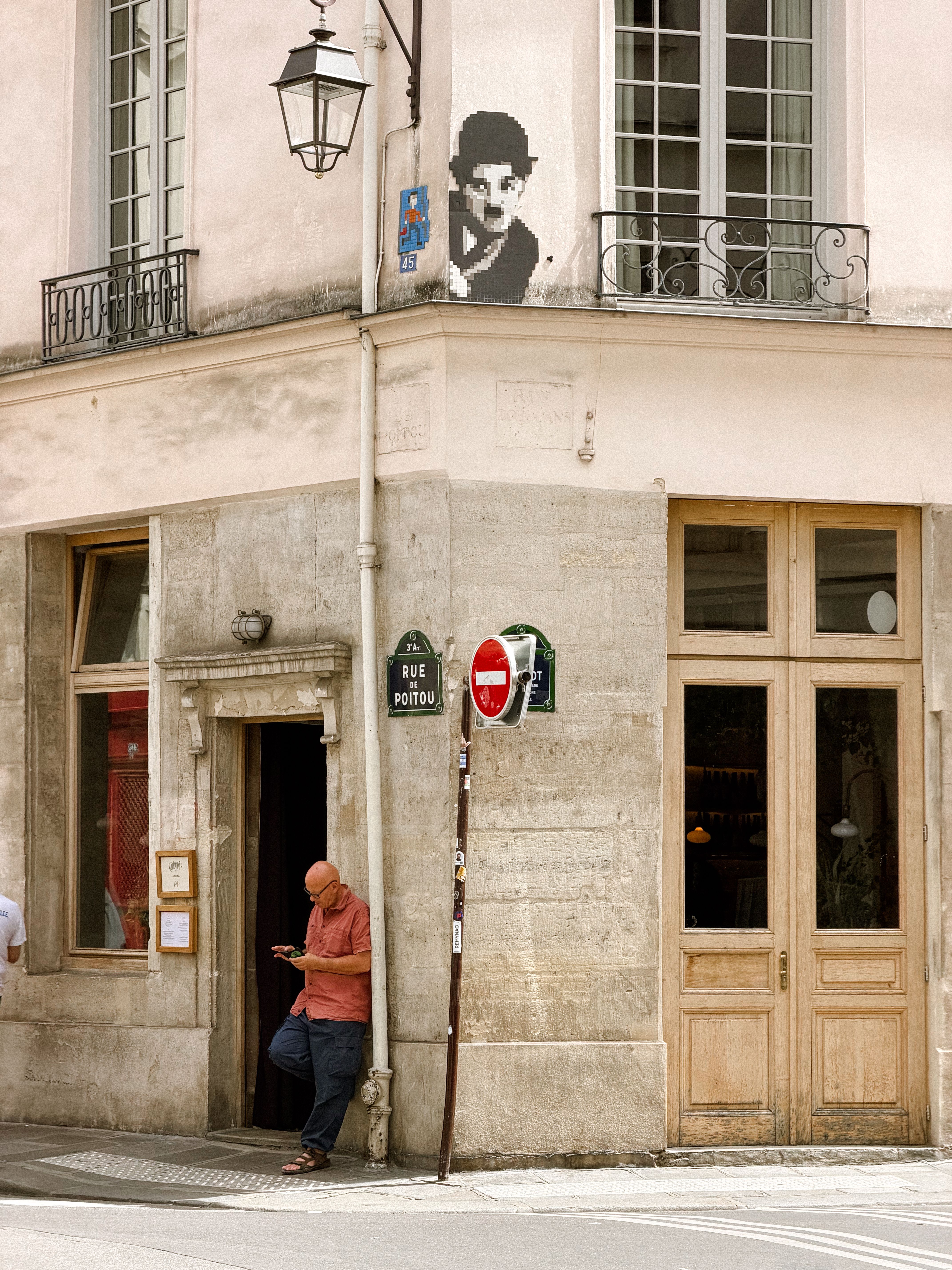 Corner street view in Paris with a man standing beneath a Charlie Chaplin mural.