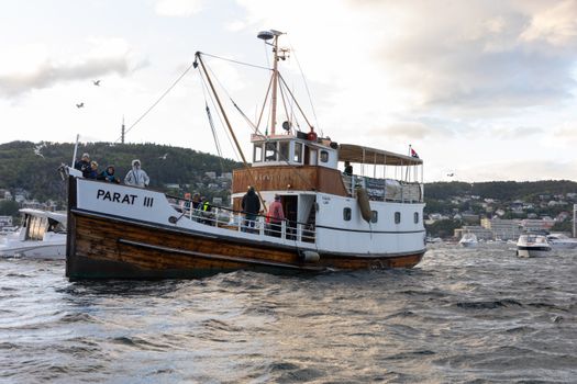 A classic wooden boat cruising through a scenic Norwegian fjord with surrounding lush landscape.