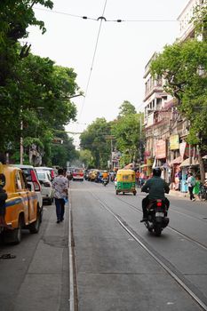 A vibrant street in Kolkata with rickshaws, cars, and pedestrians on a sunny day.