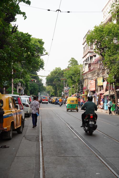 Free A vibrant street in Kolkata with rickshaws, cars, and pedestrians on a sunny day. Stock Photo