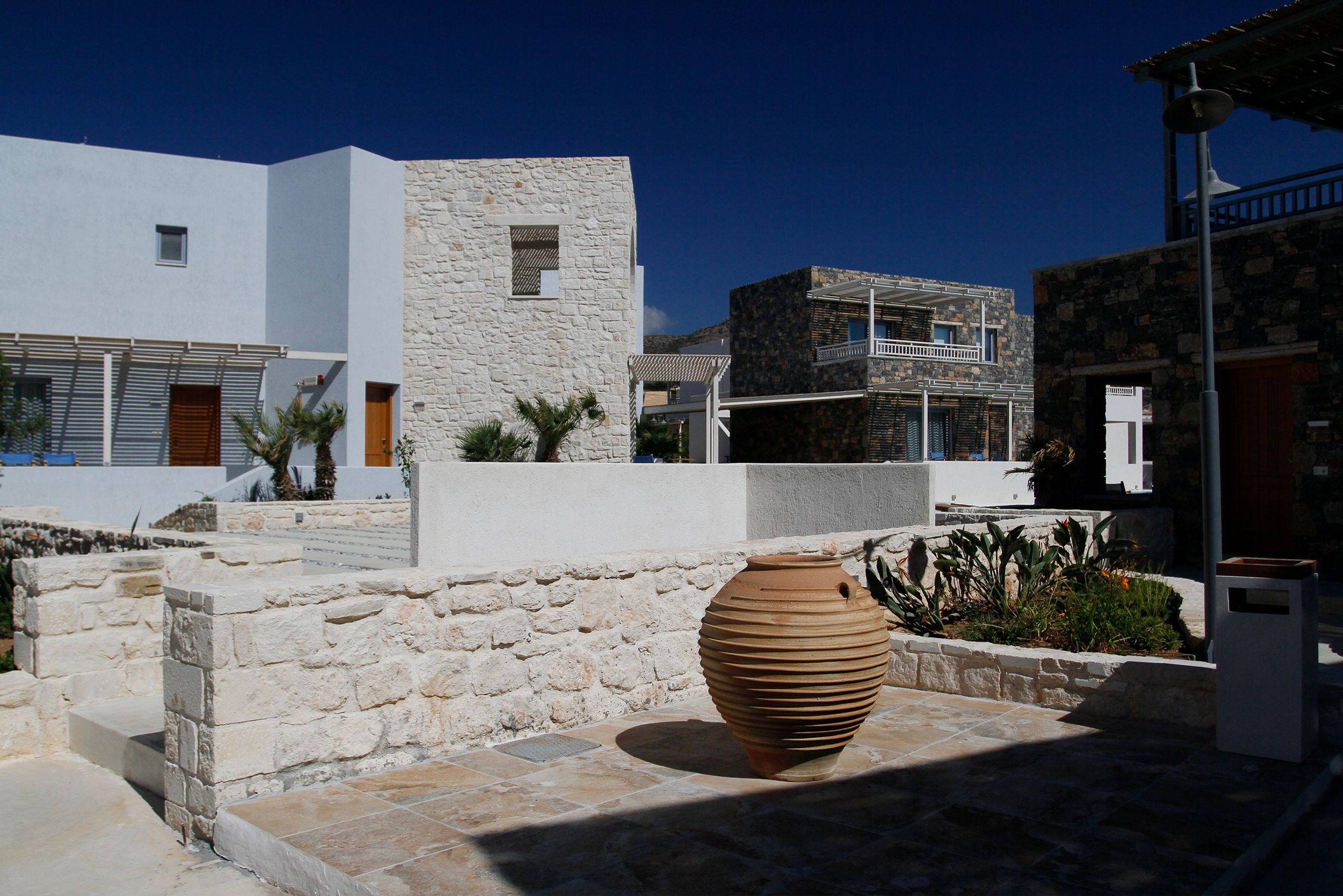 Sunlit stone courtyard featuring modern Mediterranean architecture with clear blue sky.