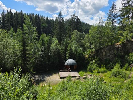 A serene forest scene featuring a unique wooden cabin under a bright blue sky.