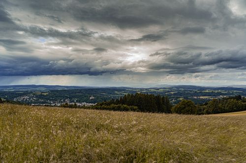 Free Panoramic view of fields and forests under a dramatic cloudy sky, showcasing nature's beauty. Stock Photo