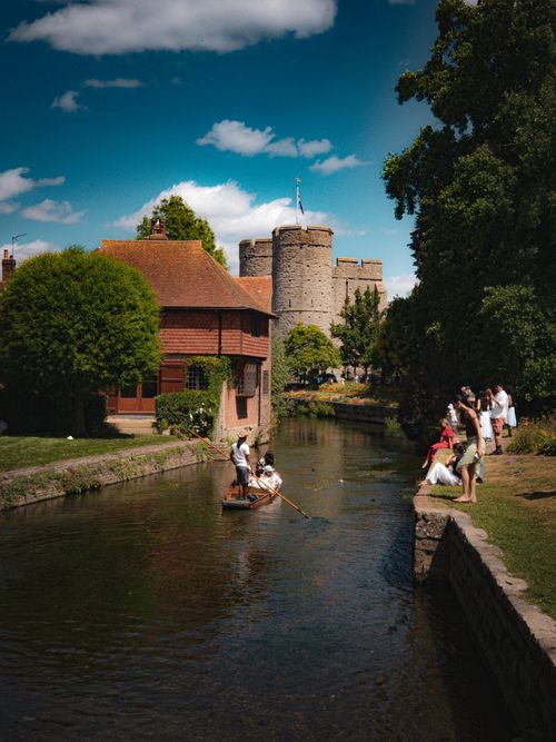 Free Idyllic summer day by a riverbank with people enjoying near a historic castle. Stock Photo