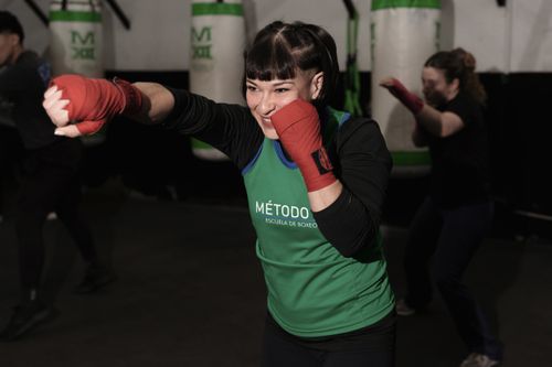 Free Energetic woman practicing boxing in a Buenos Aires gym with classmates. Stock Photo