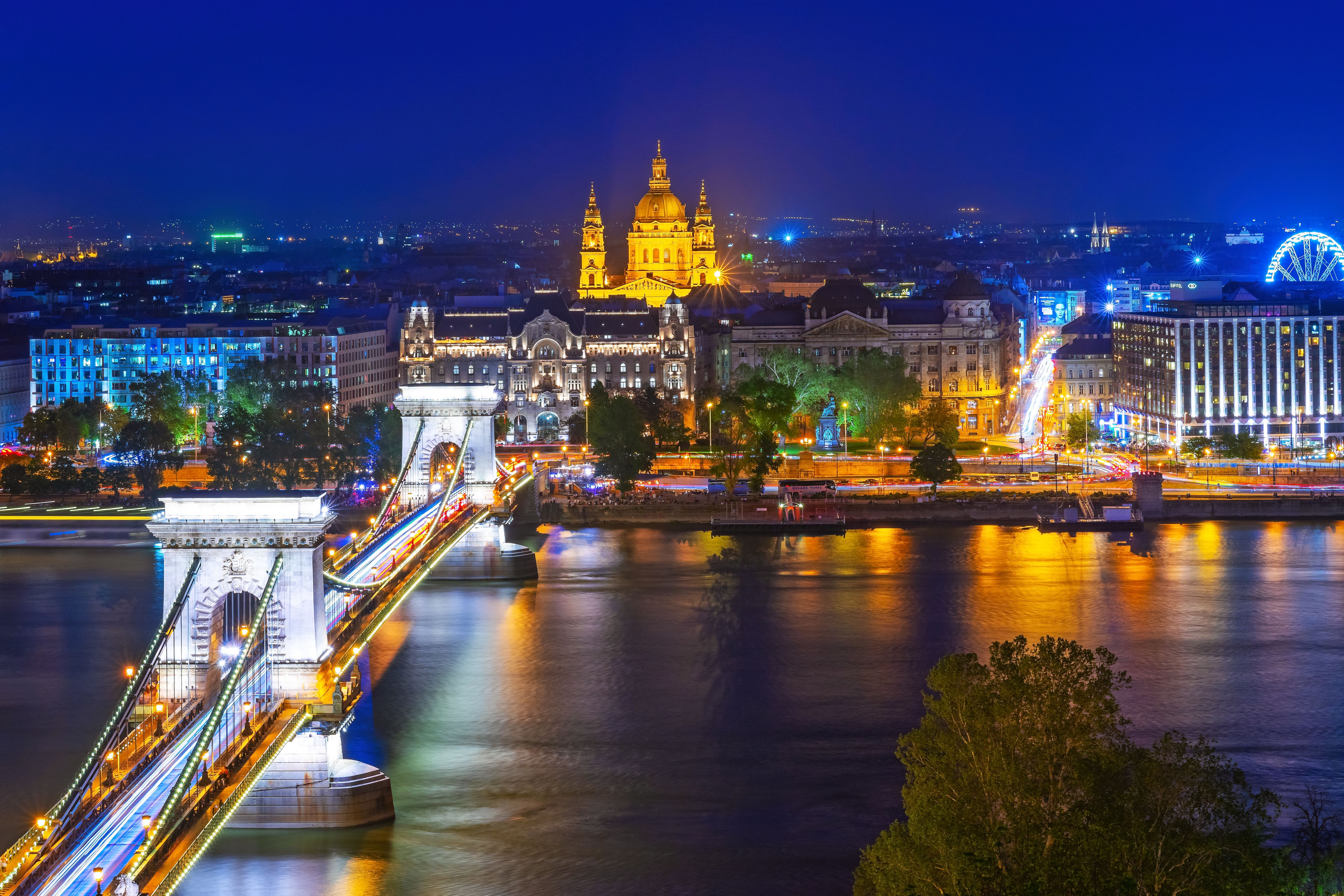 A vibrant night view of the Chain Bridge and St. Stephen's Basilica in Budapest over the Danube River.