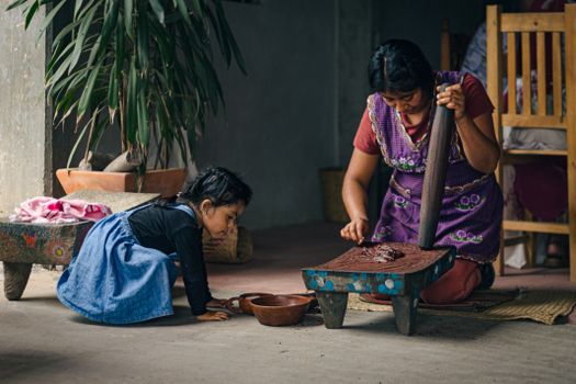 A mother and child grinding cacao indoors, showcasing traditional methods of chocolate making.