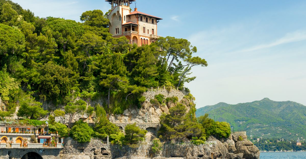 Breathtaking view of a villa perched on a green cliff in Portofino, Italy, by the vibrant blue sea.