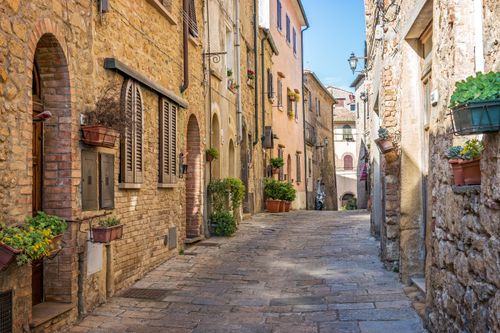 Free Explore a picturesque medieval alley with stone buildings and vibrant flowers in Tuscany's charming countryside. Stock Photo