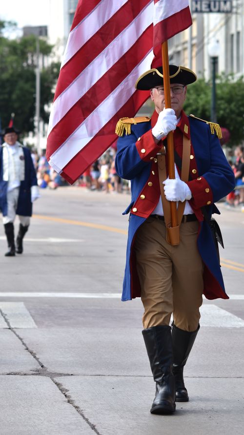 Free A historical reenactor in a military uniform holding the American flag marches in a parade. Stock Photo