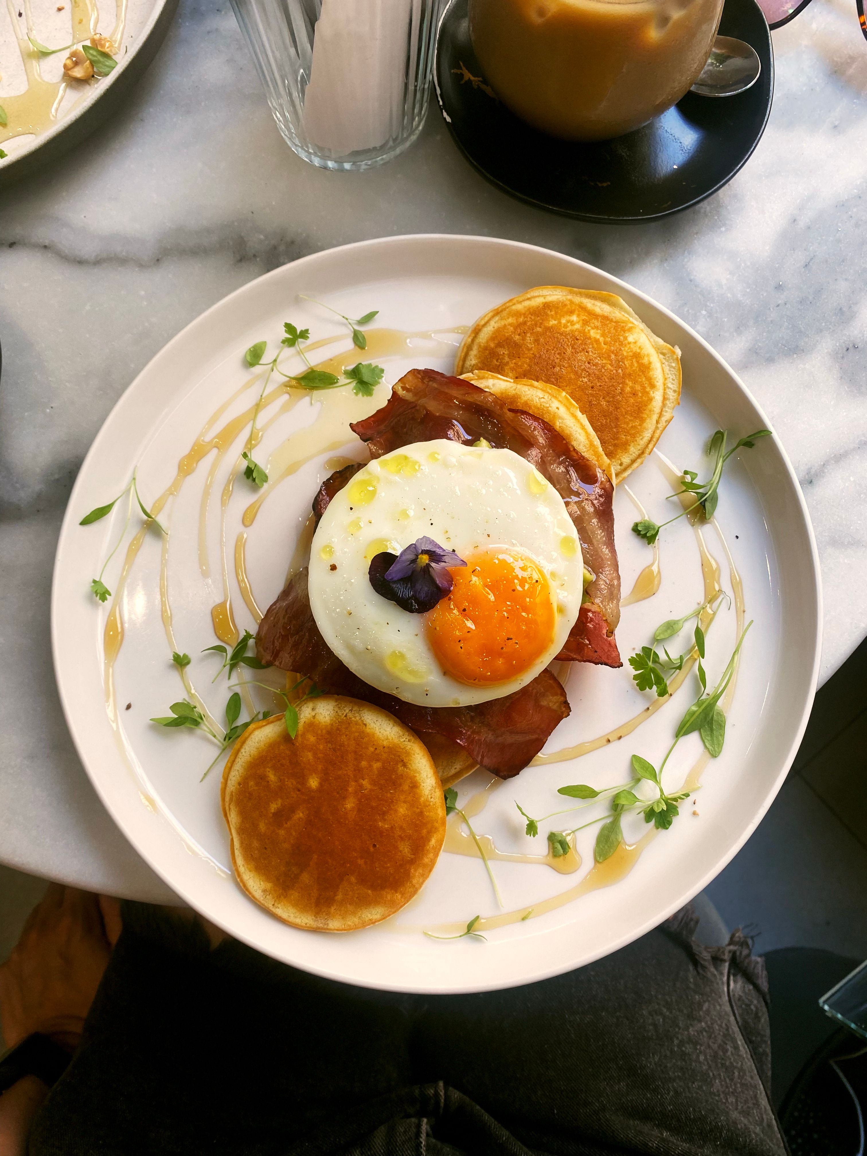 Gourmet breakfast with sunny-side-up egg, bacon, and pancakes.