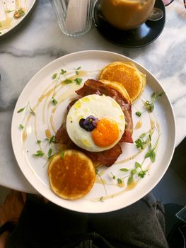 Gourmet breakfast with sunny-side-up egg, bacon, and pancakes.