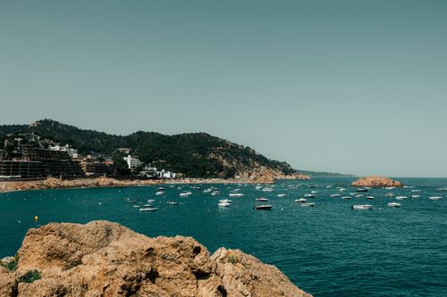 Free A picturesque scene of boats floating on the serene waters of Tossa de Mar, Spain, with lush hills and clear skies. Stock Photo