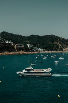A picturesque view of boats along the Tossa de Mar coastline with a tour boat in the foreground.
