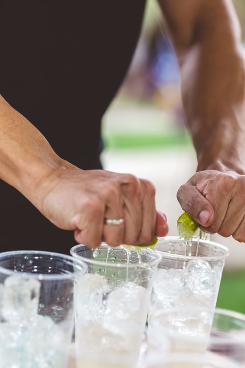 Free Close-up of hands squeezing lime into drinks with ice, outdoor setting. Stock Photo