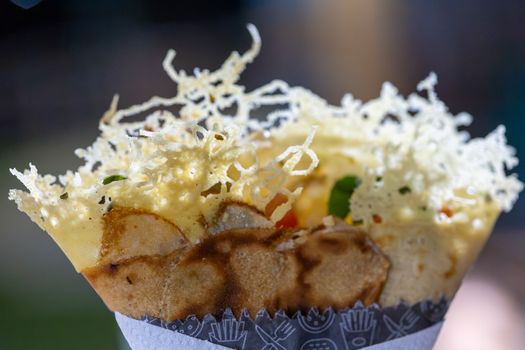 Deliciously crafted crepe topped with crispy cheese and colorful vegetables on a blurred background.