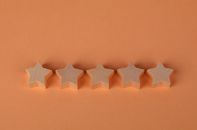 Five wooden star-shaped blocks arranged on an orange surface, perfect for rating concepts.