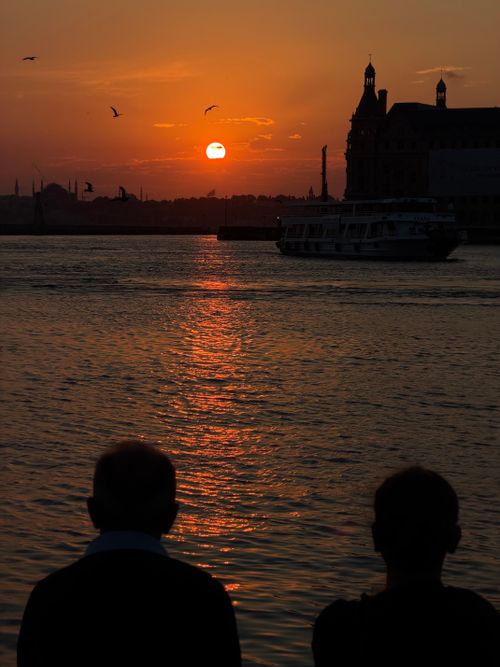 Free Silhouettes admire the sunset over Istanbul's Bosphorus, with a ferry in the foreground. Stock Photo