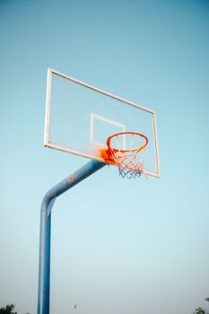 A basketball hoop with a glass backboard stands tall against a clear blue sky, perfect for sports themes.
